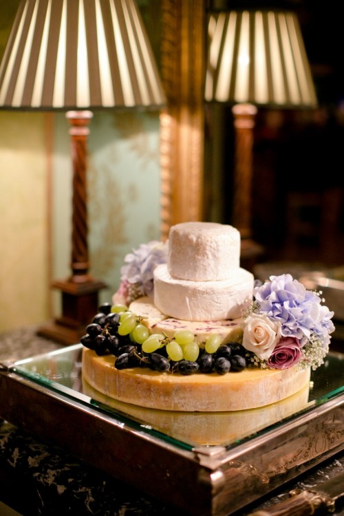 a cheese wheel tower topped with blooms and fresh grapes is a gorgeous idea for a vineyard wedding, if you don't want any sweets