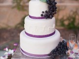 a white buttercream wedding cake with purple ribbons, a shiny monogram and grapes is a stylish solution for a fall vineyard wedding