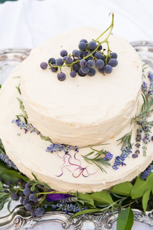 a white buttercream wedding cake topped with lavender and grapes is a lovely idea for a modern vineyard wedding that hints on the vineyard with its decor