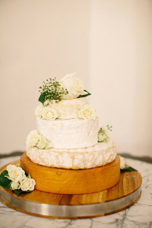 a cheese wheel tower topped with greenery and white roses is a refined and chic idea for a neutral vineyard wedding