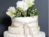 a cheese wheel wedding tower topped with greenery and white blooms is a fresh solution for those who don’t like sweets