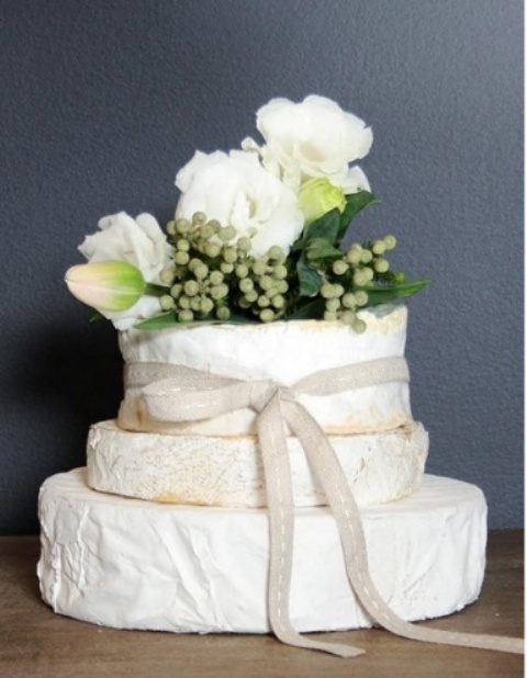 a cheese wheel wedding tower topped with greenery and white blooms is a fresh solution for those who don't like sweets