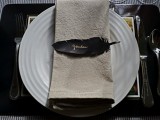 a black and white place setting with a whiet plate and neutral napkin plus a black feather place card