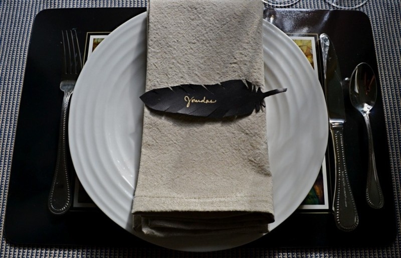 A black and white place setting with a whiet plate and neutral napkin plus a black feather place card
