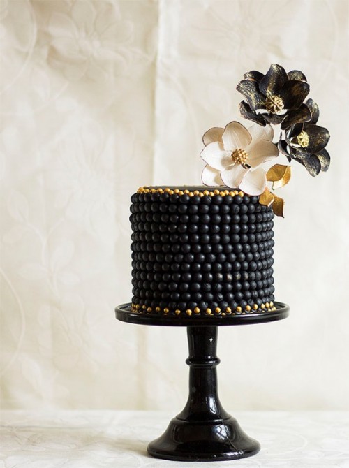 a black wedding cake decorated with beads and with black and white plus gold sugar blooms