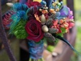 a colorful wedding bouquet in burgundy, blue, red, orange and purple, with feathers and acorns will fit a fall boho bride