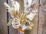 a bright summer wedding bouquet with feathers, curls and a very colorful wrap is a fun idea