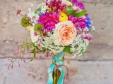 a colorful summer boho wedding bouquet with pink, peachy, white and blue blooms and some turquoise ribbons