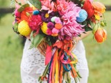 a colorful boho summer wedding bouquet in pink, red, orange, purple, with bright pompoms and colorful ribbons for a summer boho bride