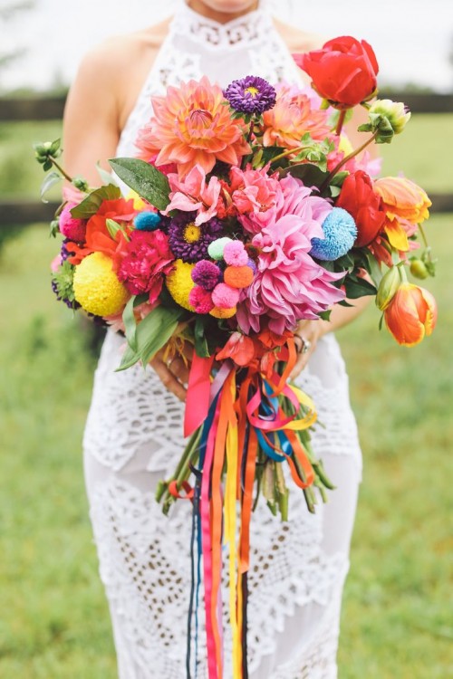 a colorful boho summer wedding bouquet in pink, red, orange, purple, with bright pompoms and colorful ribbons for a summer boho bride
