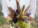 a fall wedding bouquet with deep purple blooms, green berries, feathers and dried spikes is great for a fall boho bride