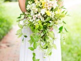 an oversized spring wedding bouquet of blush, yellow blooms and lots of greenery cascading down for a lush and bold boho look