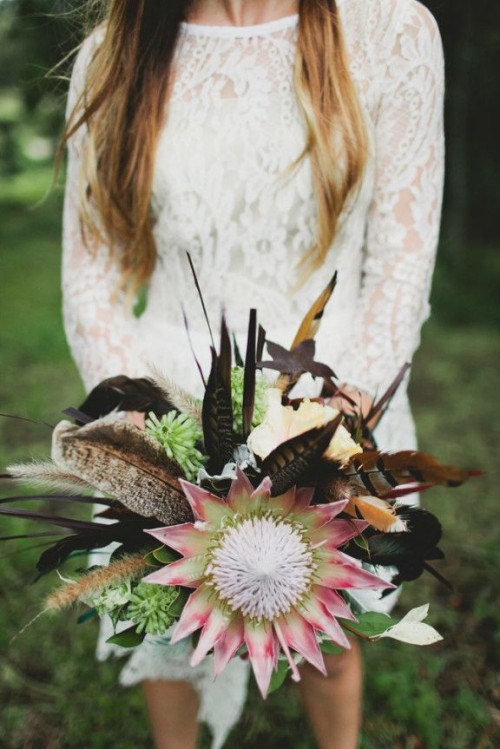 a fall boho wedding bouquet composed of succulents, feathers, spikes and king proteas looks bold
