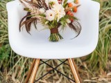 a bright fall boho wedding bouquet of neutral and orange blooms, greenery, feathers, dried touches and with a brown wrap