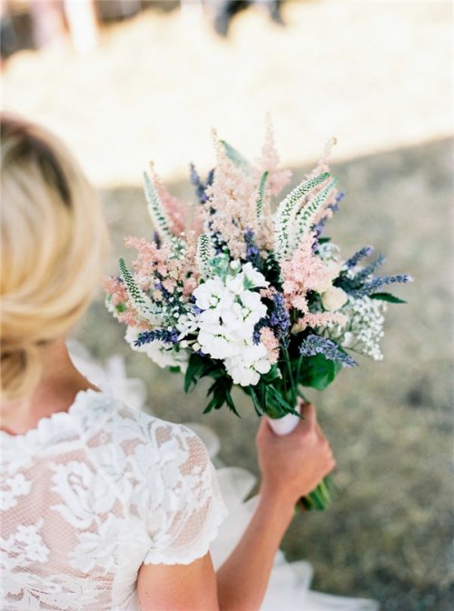 a pastel wedding bouquet in pink, blue and white with lots of greenery and other textural elements