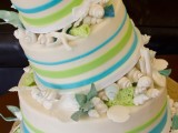 a bright wedding cake with colorful stripes, sugar seashells and starfish plus greenery looks fun and bold