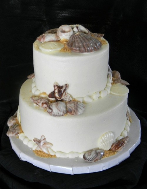 a white beach wedding cake with edible starfish, seashells, beach sand and pearls of chocolate is delicious