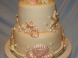 a neutral yet shimmering beach wedding cake with pink starfish and seashells, pearls and other sea creatures of sugar