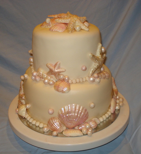 A neutral yet shimmering beach wedding cake with pink starfish and seashells, pearls and other sea creatures of sugar