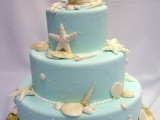 a blue beach wedding cake with pearls, seashells, starfish and a heart topper for a bright beach wedding