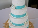 a white textural wedding cake with turquoise ribbons, sugar starfish and seashells and pearls plus beach chairs on top