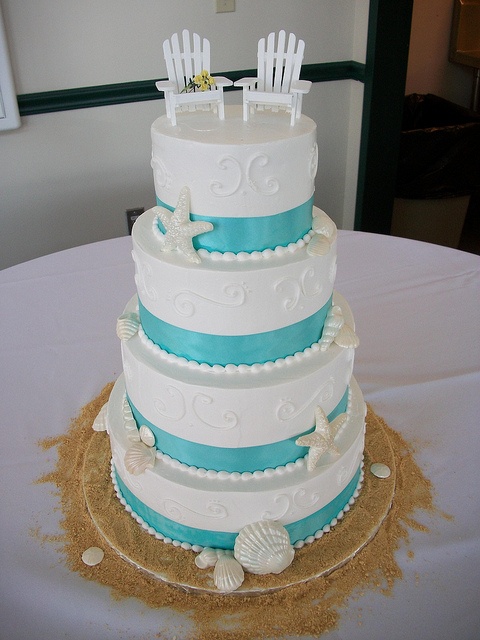 a white textural wedding cake with turquoise ribbons, sugar starfish and seashells and pearls plus beach chairs on top