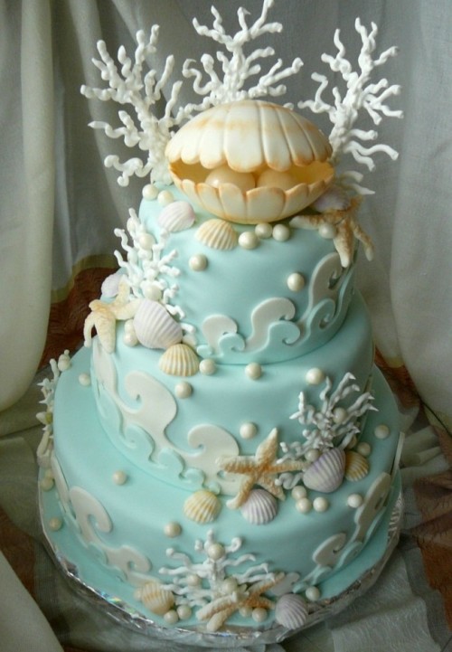 a whimsical beach wedding cake in light blue, with sugar waves, starfish, seashells, corals and a large shell on top