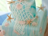 a bright watercolor turquoise wedding cake with net, starfish and seashells, all made of sugar