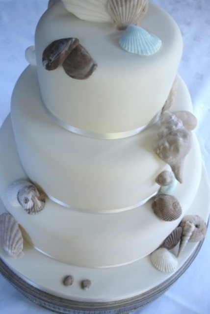 a plain white wedding cake with real and sugar seashells in grey for a minimalist beach wedding
