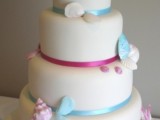 a plain white wedding cake with blue and pink ribbons, with pink and blue sugar seashells and starfish is a chic and fun idea for a beach wedding