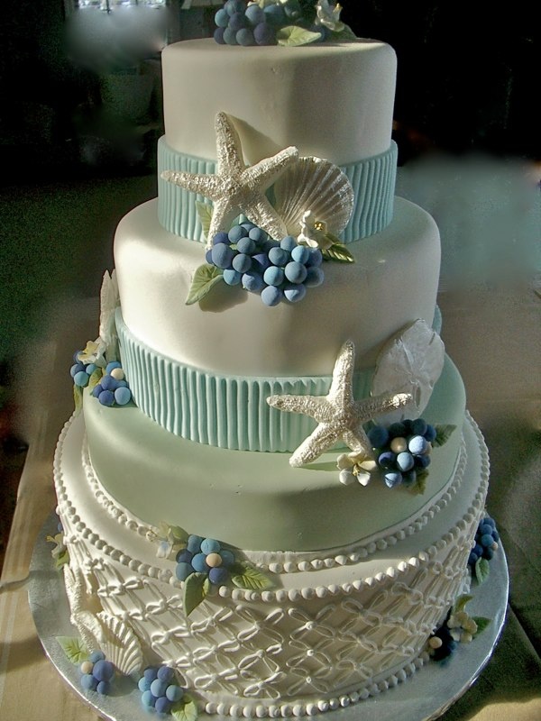 A shiny white wedding cake with light blue ribbons, sugar berries, starfish, patterns looks very quirky and unusual