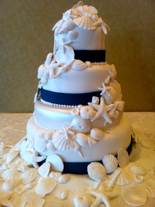 a nautical wedding cake in white, with navy ribbons, sugar seashells, starfish and urchins is very bold and contrasting