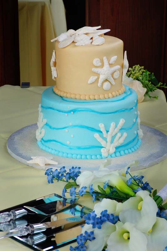 A bright beach wedding cake with a tan and bright blue tier, sugar corals, seashells and starfish for a beach wedding