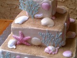 a catchy blush square wedding cake with beach sand, seashells, corals and starfish of sugar in various colors