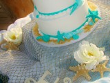 a white wedding cake with bright turquoise starfish and seashells for a bold beach wedding