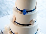 a white wedding cake with navy ribbons, sugar seashells, pearls, blue flowers is amazing for a bold beach or nautical wedding