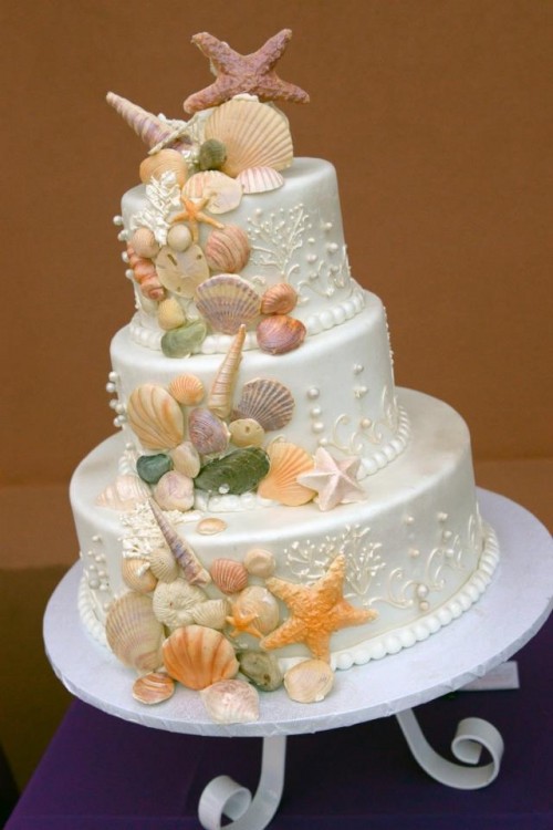 a white shimmering wedding cake with colorful sugar seashells, starfish and pearls is a bold and fun option for a modern beach wedding