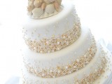a whimsical beach wedding cake in white, with copper, gold and white pearls attached and sugar seashells and starfish on top
