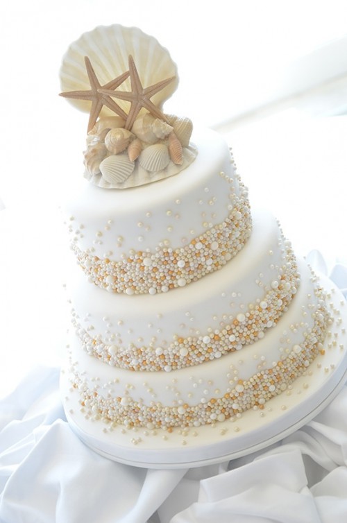 a whimsical beach wedding cake in white, with copper, gold and white pearls attached and sugar seashells and starfish on top