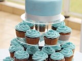 a plain blue wedding cake topped with sugar seashells and matching cupcakes with blue icing for a stylish beach wedding