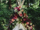 a romantic teepee decorated with lush and bold blooms and greenery and with pillows inside is a lovely and chic idea