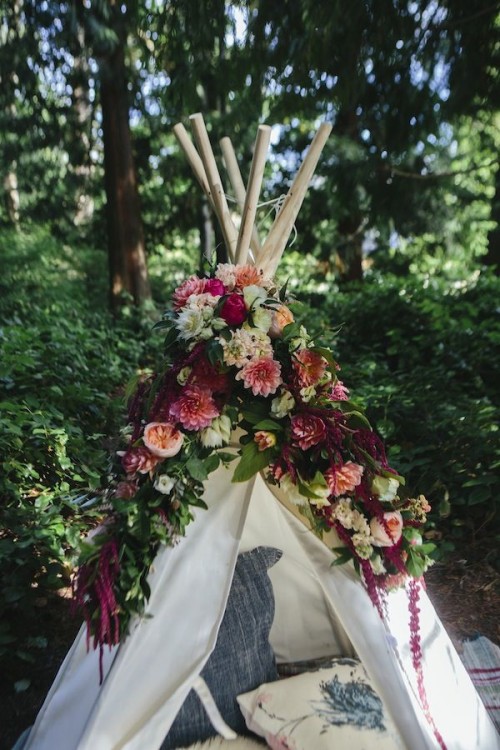 a romantic teepee decorated with lush and bold blooms and greenery and with pillows inside is a lovely and chic idea