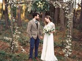 a boho woodland wedding arch covered with leaves and neutral blooms and some crystals is a very pretty idea