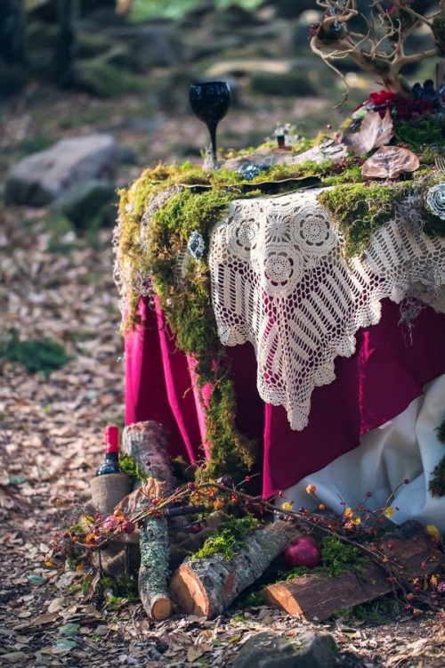 a beautiful boho woodland wedding tablescape with layered linens - lace, bold colored and moss ones, a tree with dark blooms and leaves and some firewood