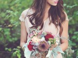 a boho woodland bride wearing a blush pleated wedding dress with lace cap sleeves, a boho chain on the head and carrying a very bold floral bouquet