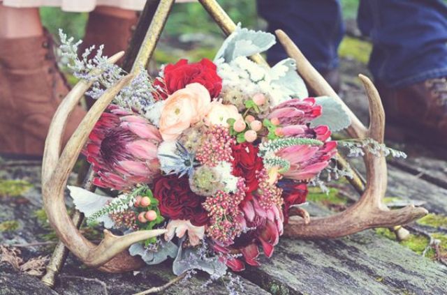 a bright boho woodland wedding centerpiece of bold flowers, pale leaves and antlers looks wild and pretty