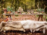 a boho woodland wedding tablescape with a fur covered bench, potted greenery, antlers, woven candle lanterns, fruits and leaves is a lovely and chic idea