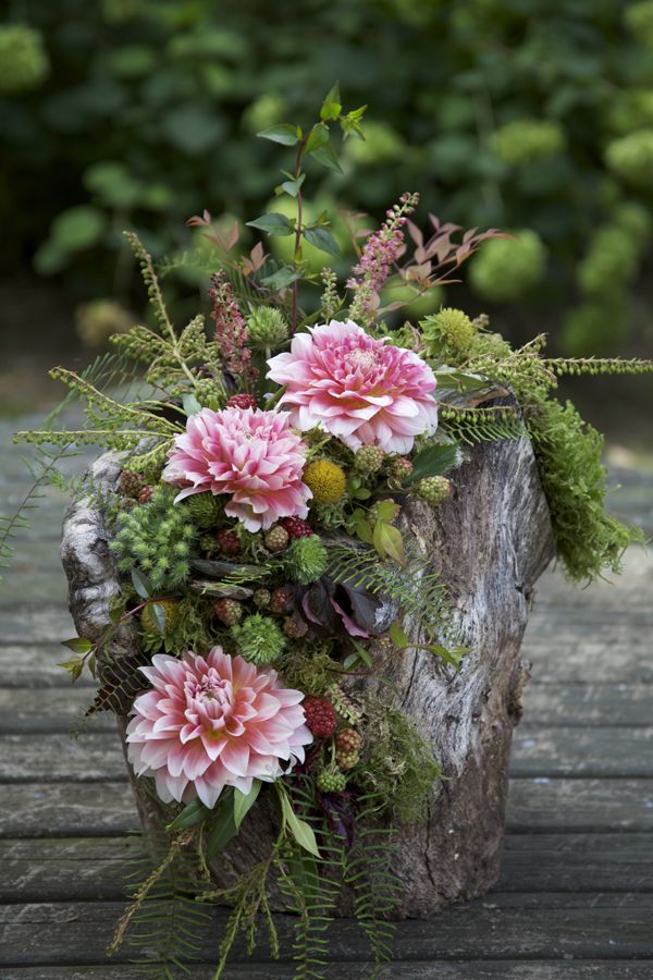 A tree stump decorated with lush greenery, pink blooms and berries is  lovely boho woodland decoration or a centerpiece
