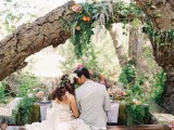 a boho woodland wedding reception space with lush moss, greenery, bold blooms and boho pillows plus some decor over the table