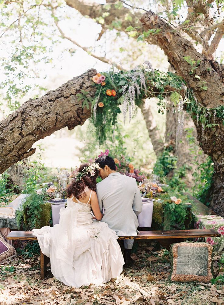 A boho woodland wedding reception space with lush moss, greenery, bold blooms and boho pillows plus some decor over the table